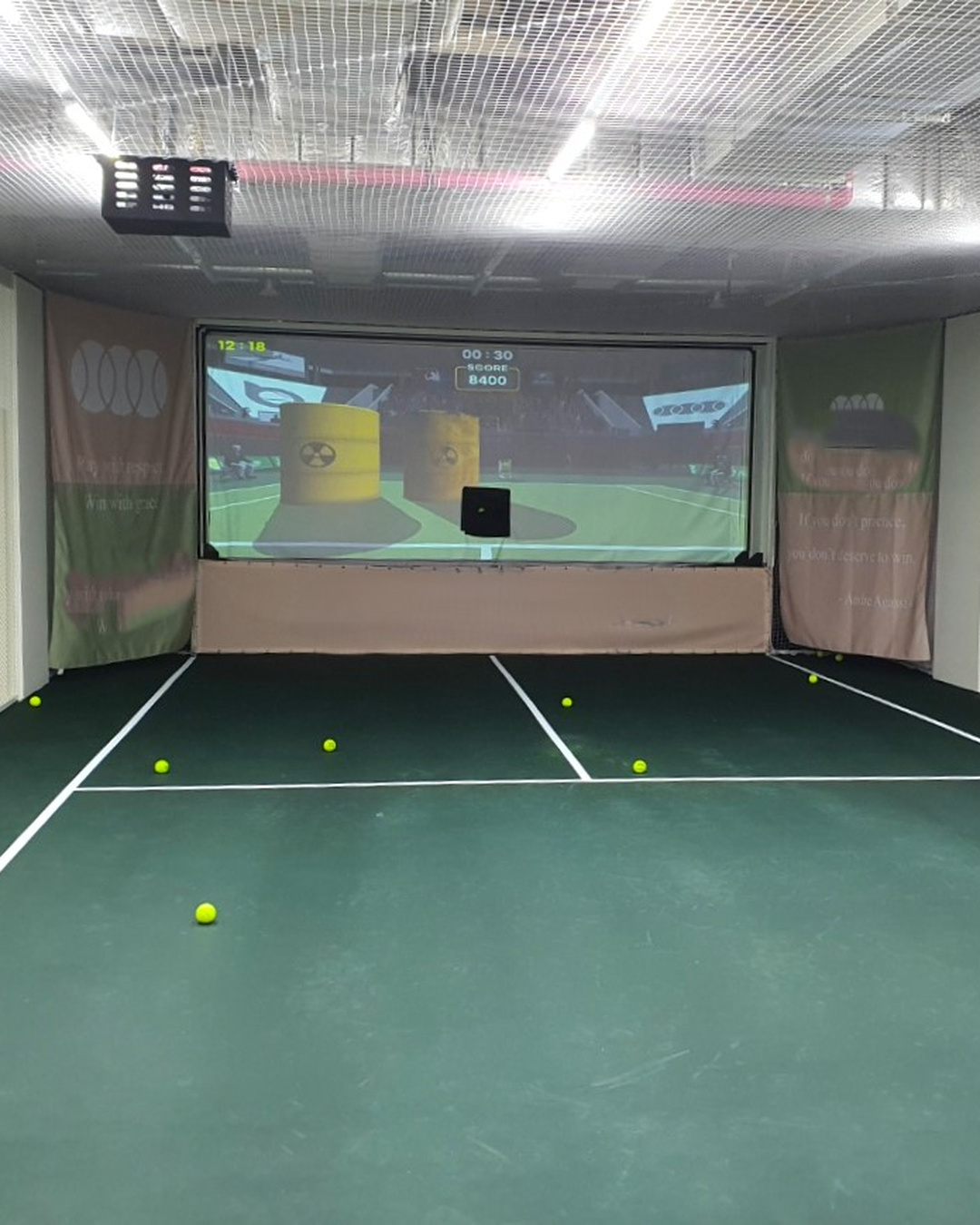 Indoor tennis simulator court with a projected training game and tennis balls.